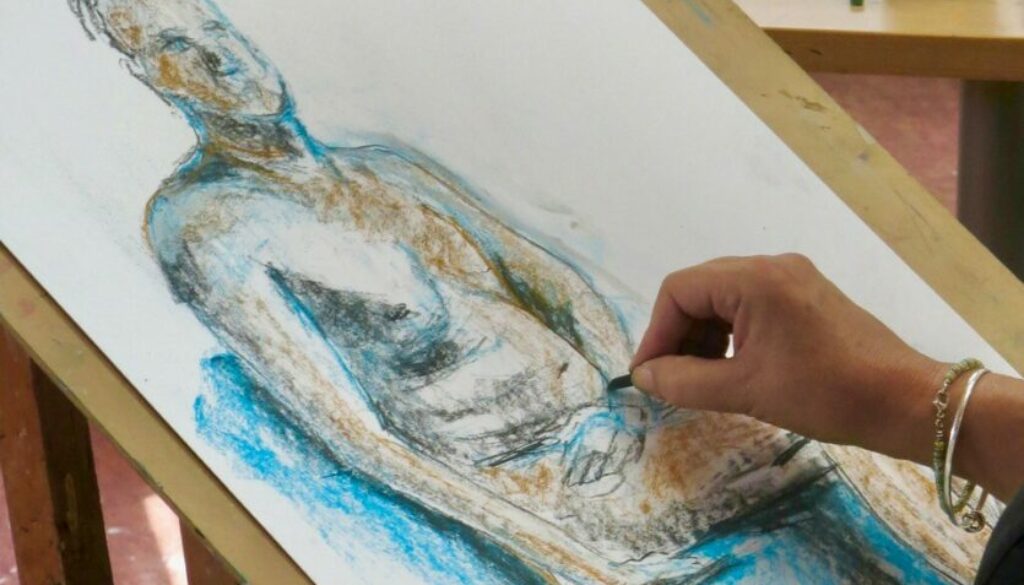 artists hands drawing a pastel sketch of a nude man