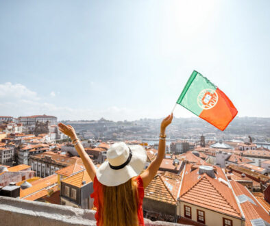 Young woman tourist in red dress standing back with portuguese flag